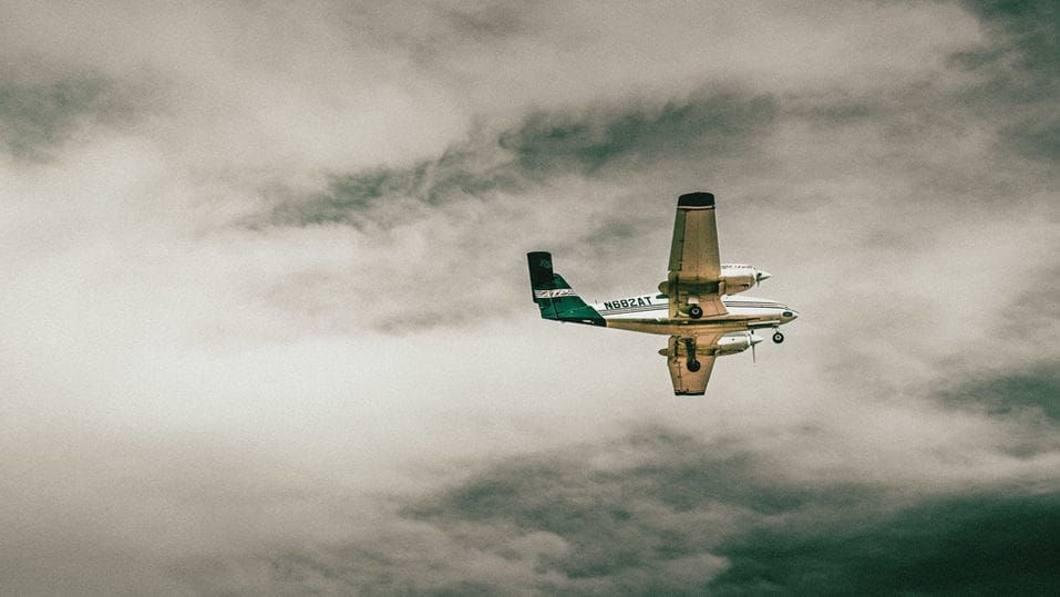 Twin-engine propeller plane banking through heavy grey clouds